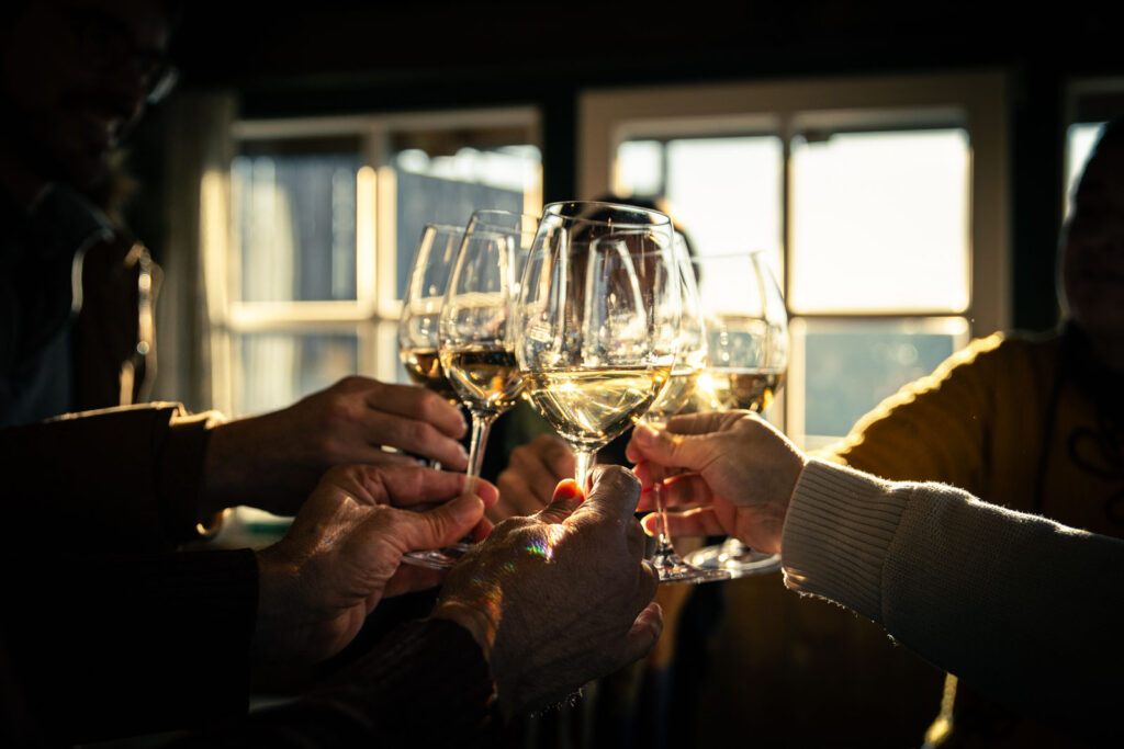 Gent amb copes de vi a les mans fent un brindis amb el sol a contrallum
